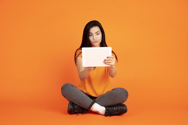 Caucasian young woman's portrait on orange studio background.