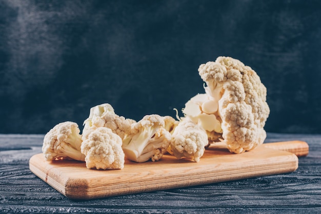 Cauliflower in a cutting board on a dark wooden table. side view.