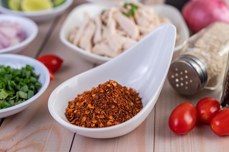 Free Photo cayenne chili in a white spoon, tomato placed on a wooden table.