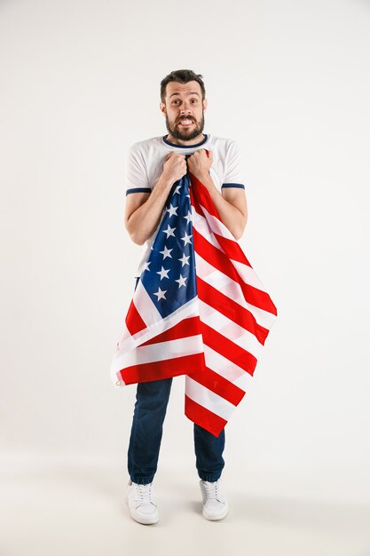 Celebrating an Independence day. Stars and Stripes. Young man with flag of the United States of America isolated on white studio wall. Looks crazy happy and proud as a patriot of his country.