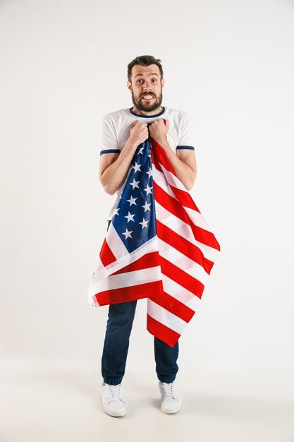 독립 기념일을 축하합니다. 별과 줄무늬. 화이트 스튜디오 벽에 고립 된 아메리카 합중국의 국기와 함께 젊은 남자. 그의 나라의 애국자로서 미친 행복하고 자랑스러워 보입니다.