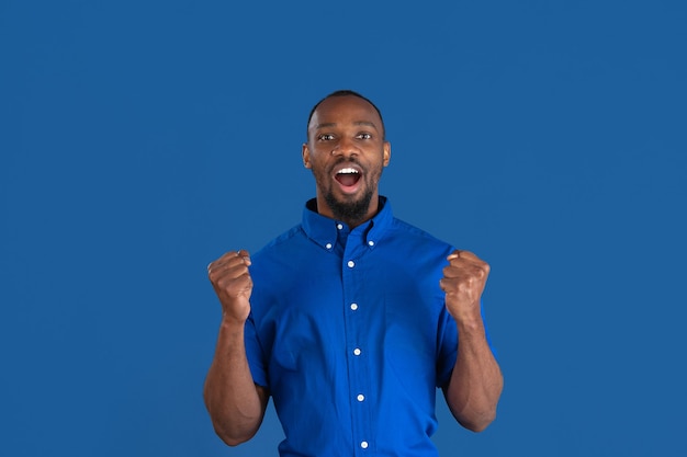 승리를 축하합니다. 파란색 벽에 고립 된 젊은 아프리카 계 미국인 남자의 흑백 초상화. 아름다운 남성 모델. 인간의 감정, 표정, 판매, 광고 개념. 청소년 문화.