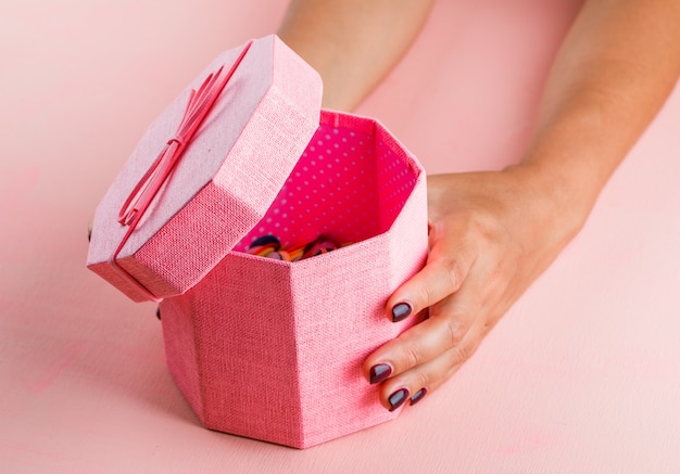 Celebration concept on pink table high angle view. woman opening gift box.