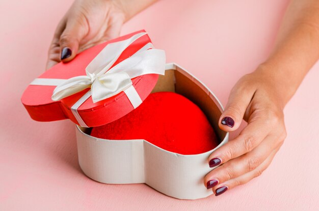 Celebration concept on pink table high angle view. woman opening gift box.