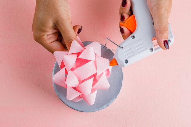 Celebration concept with gift box on pink table flat lay. woman using glue gun.