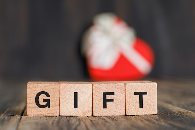 Celebration concept with gift box, wooden cubes on wooden table side view.