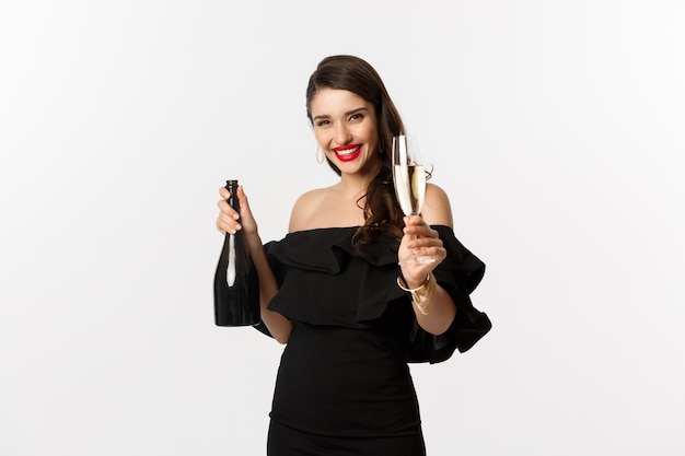 Celebration and party concept. Happy woman enjoying New Year, raising glass of champagne and saying toast, standing in black dress over white background