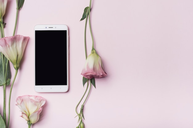 Foto gratuita telefono cellulare con i fiori di eustoma contro fondo rosa