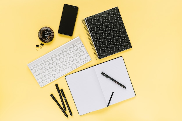 Мобильный телефон и белая клавиатура с канцелярскими принадлежностями на желтом фоне