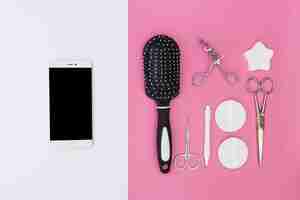 Free photo cellphone and cuticle; hair brush; scissors; sponge; eyelash curler and sponge on dual backdrop