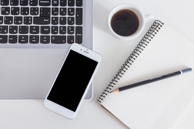 Cellphone on laptop with cup of coffee and pencil over the notebook