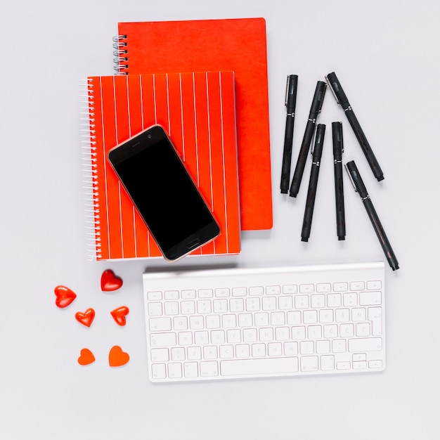赤いカバーのスパイラルノートの携帯電話;ペンとハート型キャンディー、白いキーボード