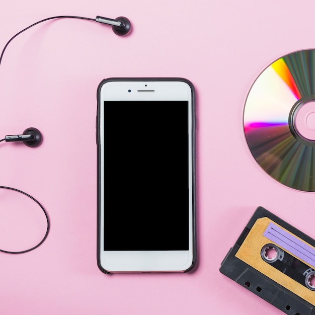 Cellphone with earphone; disc and cassette on pink background