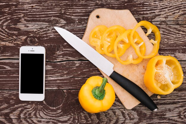 Cellphone with yellow bell pepper and knife on wooden desk