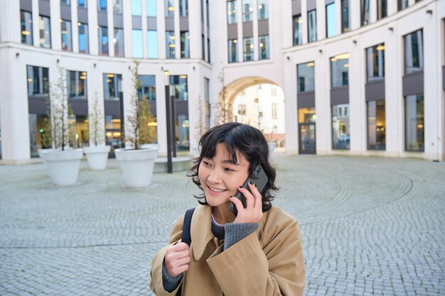 Foto gratuita la tecnologia cellulare giovane donna coreana parla al cellulare fa una telefonata mentre torna a casa a piedi