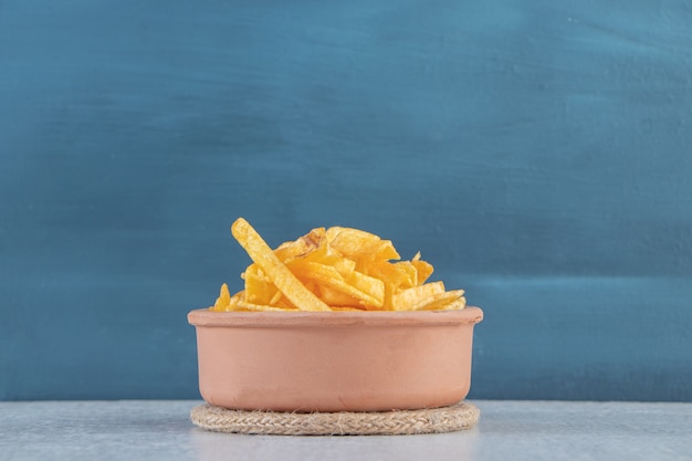 Ceramic bowl of crispy potato sticks on stone.