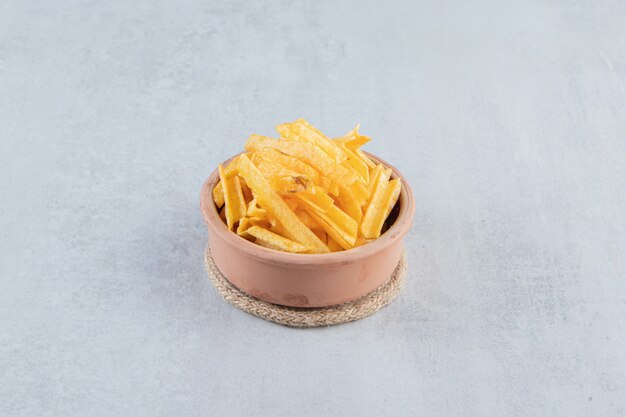 Ceramic bowl of crispy potato sticks on stone.