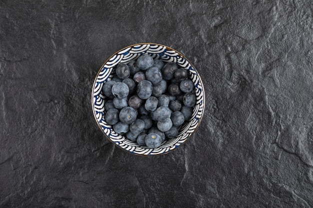 Ceramic bowl of delicious fresh blueberries on black surface