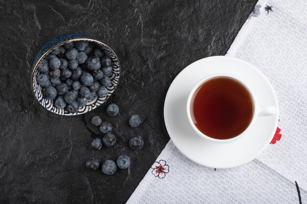 黒い表面においしい新鮮なブルーベリーとお茶のセラミックボウル