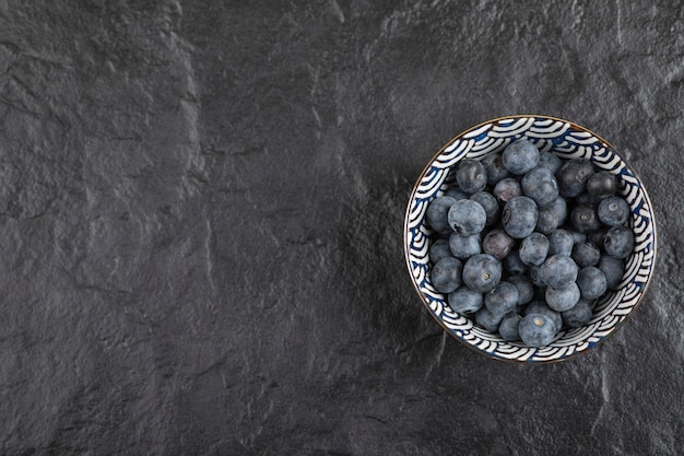 Ceramic bowl of delicious ripe blueberries on black surface