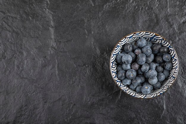 Ceramic bowl of delicious ripe blueberries on black surface