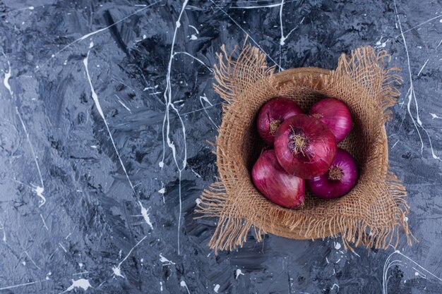 Ceramic bowl of fresh red onions on blue background.
