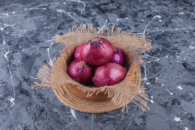 Ceramic bowl of fresh red onions on blue surface