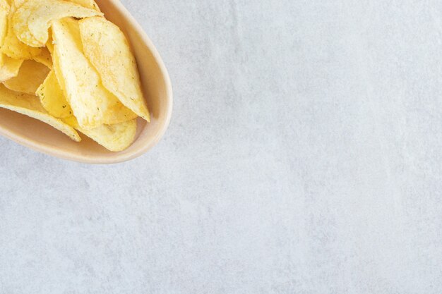 Ceramic bowl of salted crispy chips on stone.