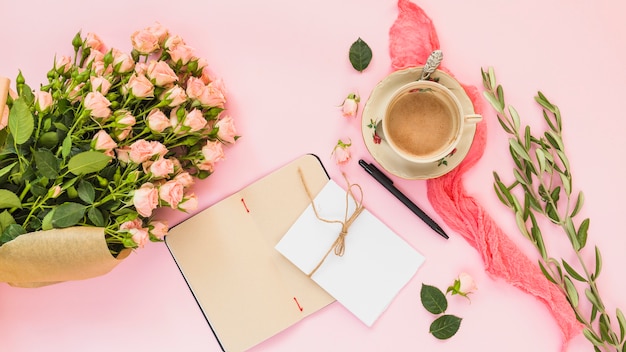 세라믹 커피 컵; 장미 꽃다발; 분홍색 배경에 일기와 카드