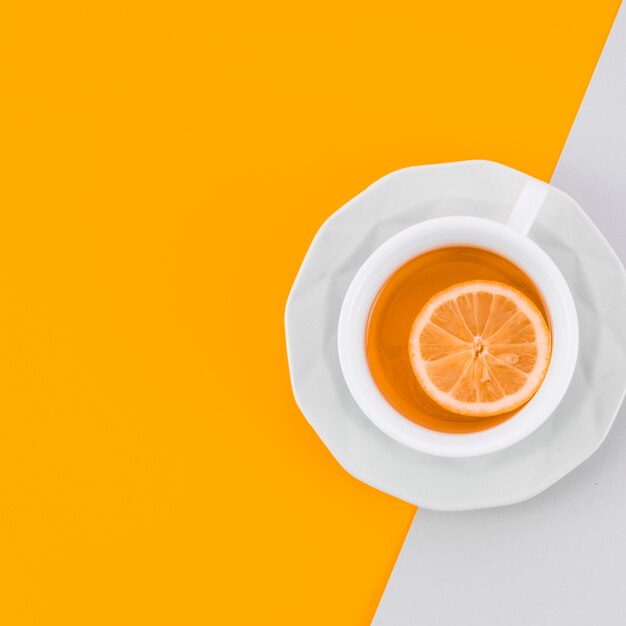 Керамическая чашка имбирного чая с лимоном на желтом и белом фоне