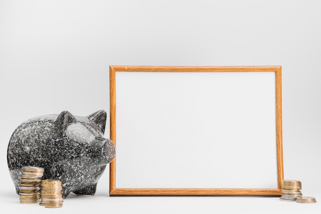 Ceramic piggybank with stack of coins near the white board against white background