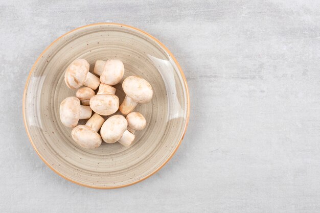 Ceramic plate of fresh uncooked mushrooms on stone table. 
