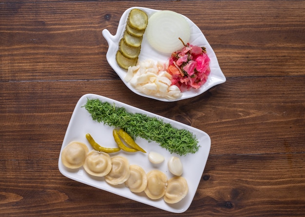 Ceramic plate full of homemade dumplings and pickles on wooden surface.
