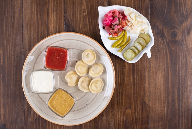 Керамическая тарелка с домашними клецками и солеными огурцами на деревянной поверхности.