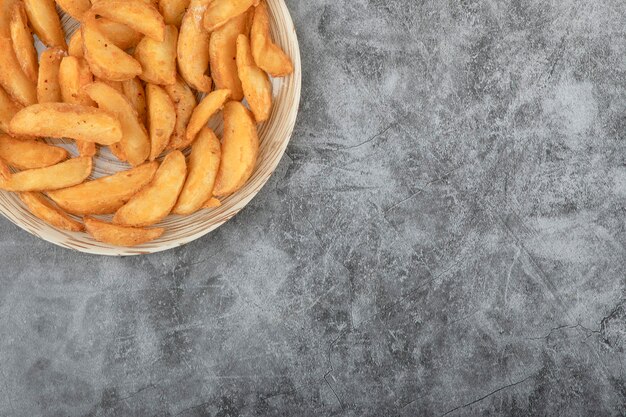 Керамическая тарелка вкусных жареных картофельных дольков на каменном фоне.