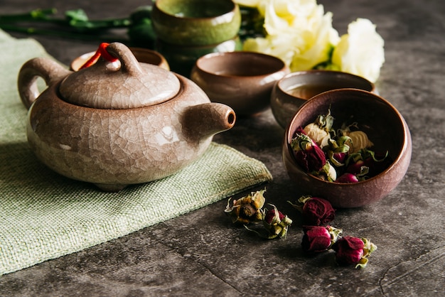 Ceramic traditional teapot with teacups and dried rose on concrete backdrop