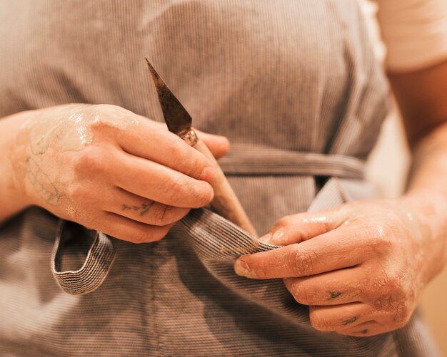 Ceramist hands holding a carving tool from the pocket