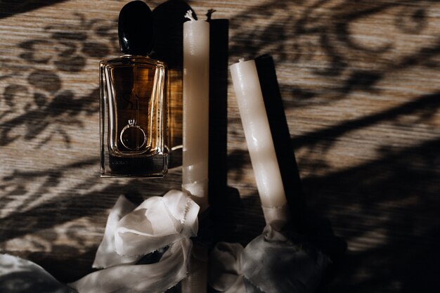 Ceremonial wedding candles with white ribbons, engagement ring and perfume on the wooden floor