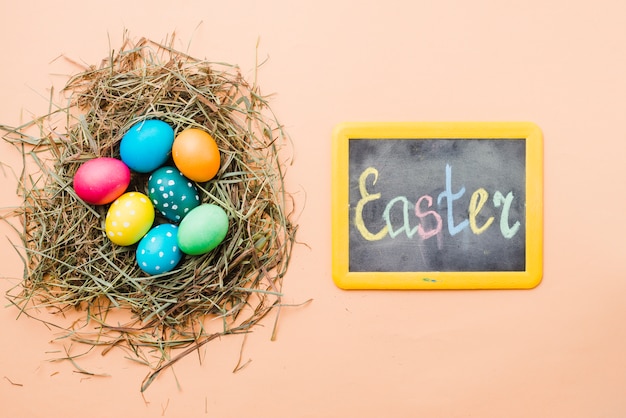 Free photo chalkboard with easter title near set of bright colored eggs in nest