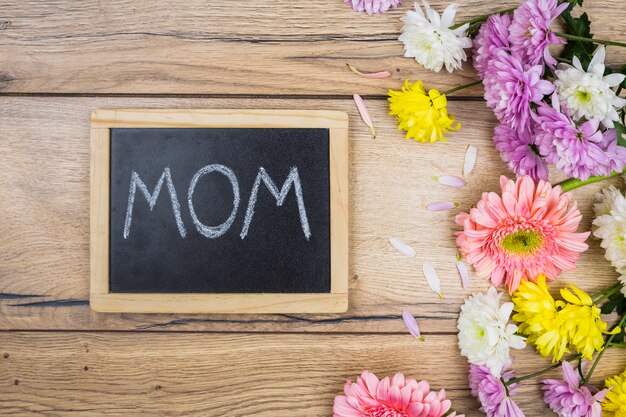 Chalkboard with mom title near fresh bright flowers on desk