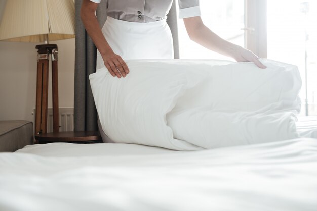 горничная заправляет кровать в гостиничном номере