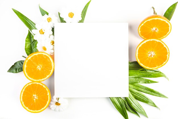Ромашки и апельсины возле листьев и бумаги