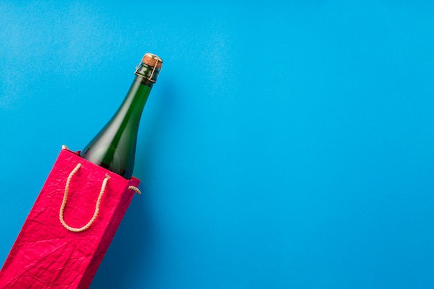 Champagne bottle in bright red paper bag on blue surface