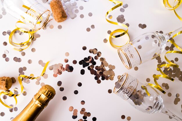Champagne bottle with empty glasses; confetti and streamers on white background