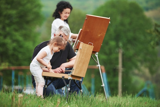 Changing colors. Grandmother and grandfather have fun outdoors with granddaughter. Painting conception