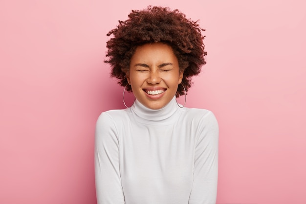 Free photo charismatic carefree woman laughs from hilarious joke, closes eyes, shows perfect teeth