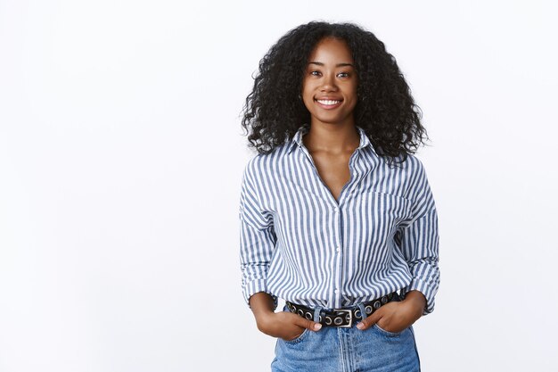 Charismatic cheerful attractive african american woman curly haircut wearing shirt holding hands pockets confident outgoing smiling, talking pleasant conversation, feeling self-assured relaxed