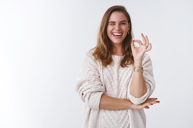 Free photo charismatic confident upbeat gorgeous adult woman wearing loose stylish sweater cozy winking flirty sassy smiling broadly showing okay ok gesture excellent mood assuring everything awesome