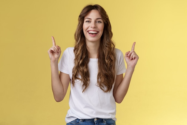 Charismatic enthusiastic attractive lively woman having fun enjoy awesome night out party laughing joyfully pointing up index fingers up introduce promo smiling happily yellow background