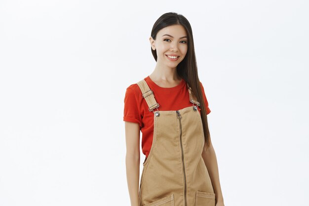 charismatic happy and relaxed modern asian female in brown overalls with dark long hair smiling friendly